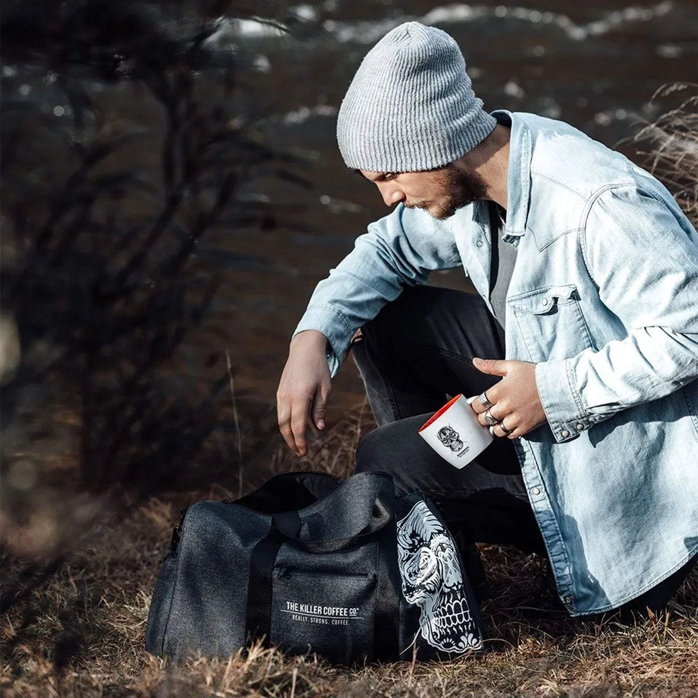 Person sitting outdoors with a black bag featuring a skull design and a branded coffee cup.