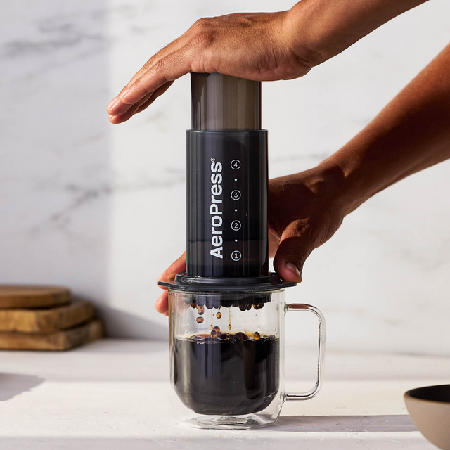 Hands pressing an AeroPress Original into a glass mug on a marble bench