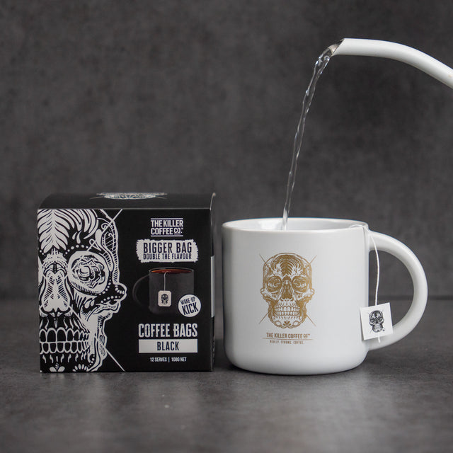 Hot water pouring into a Killer mug beside a box of Black Dunk Coffee Bags