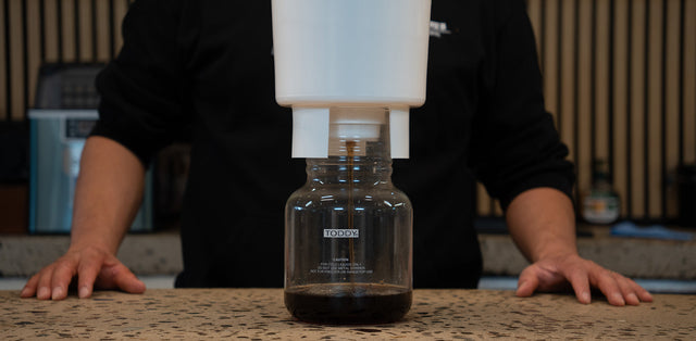 Toddy cold brew system brewing concentrate into its glass decanter on a stone bench
