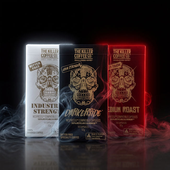 Three coffee capsule packages from The Killer Coffee Co. are lined up on a dark reflective surface with dramatic colored lighting.